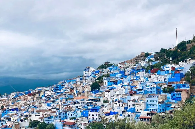 Le case blu e bianche di Chefchaouen distese su un pendio verde sotto le nuvole