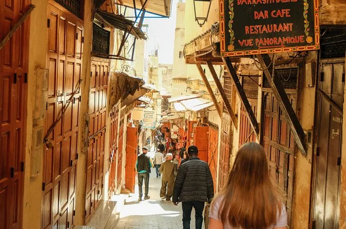 A narrow covered souk street in the Fes medina with wooden doors and shop signs