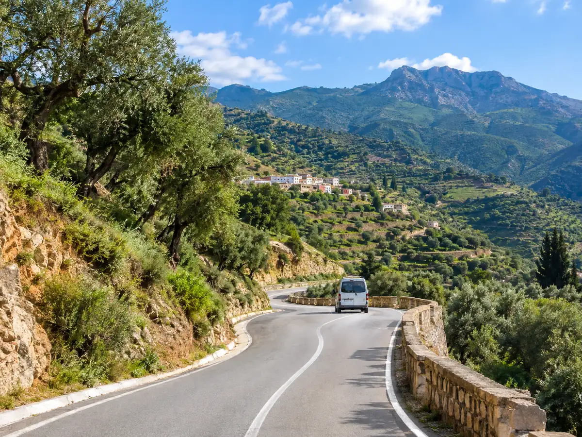 Un minivan su una strada di montagna tortuosa sopra valli verdi